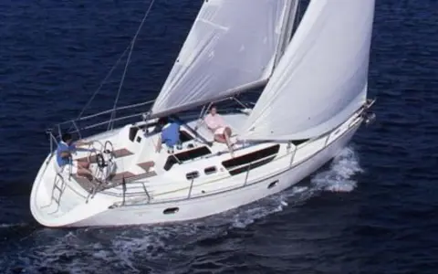 Trois personnes profitent d'une belle journée en mer à bord de voiliers occasion 9 10 mètres. Le bateau blanc navigue sur des eaux bleues.