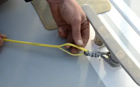 Main d'un marin préparant la ligne de vie d'un voilier, sécurisant une amarre sur un taquet.