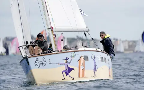 Un bateau muscadet décoré de personnages fantaisistes navigue sur l'eau, avec deux hommes à bord.