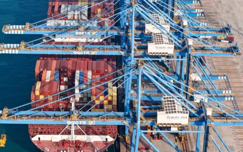Grands portiques bleus en action, chargeant des conteneurs sur un navire. La capacité porte conteneur est impressionnante, montrant la logistique mondiale.