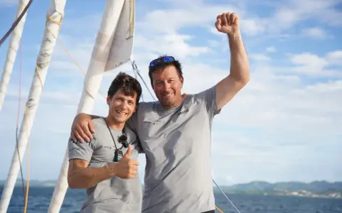 Guillaume Pirouelle et son coéquipier célèbrent une victoire sur l'eau, bras levés et souriants, sous un ciel bleu.