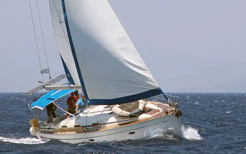 Un voilier blanc navigue sur une mer bleue agitée. L'équipage semble prendre un ris, ajustant les voiles pour mieux affronter le vent.