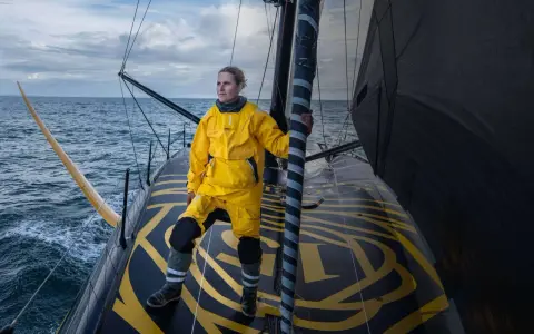 Clarisse Crémer, en tenue de voile jaune vif, se tient fièrement sur le pont d'un voilier, prête à affronter les éléments.