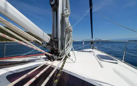 Vue de l'avant d'un voilier naviguant sur une mer bleue. Les cordages sont bien rangés, prêts à hisser le grand mât.