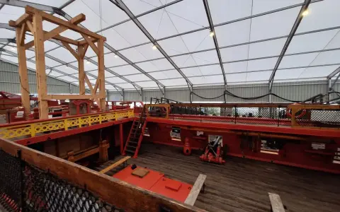 L'intérieur du **bateau Hermione** est en cours de restauration. On voit la structure en bois, les ponts rouges et jaunes, et un canon.