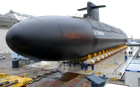 Le sous-marin "Le Terrible" est en cours de construction, sa taille impressionnante est mise en valeur sur des supports jaunes.
