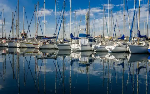 Une flotte de voiliers anglais, leurs mâts élancés se reflétant sur l'eau calme d'un port sous un ciel bleu éclatant.