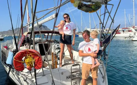 Famille souriante sur un voilier, prête pour une aventure transatlantique à voile.