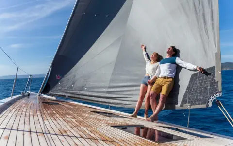 Un couple heureux profite du soleil sur un voilier. Ils semblent avoir fait le bon choix en décidant de choisir un voilier pour leurs vacances.