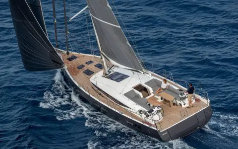 Un couple profite d'une croisière sur un voilier habitable à l'année, naviguant sur des eaux bleues par une journée ensoleillée.