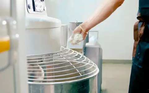 Main d'un boulanger ajoutant de la pâte à un pétrin, partie intégrante de l'entretien du matériel en cuisine.
