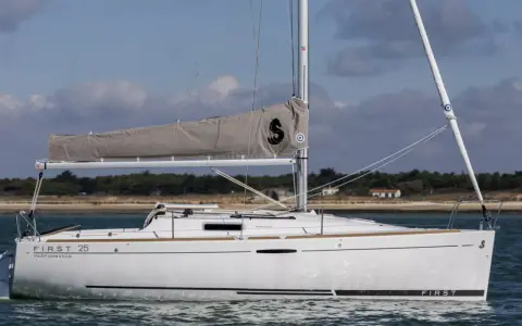 Voilier blanc "First 25 Performance" naviguant sur une mer calme, avec une voile grise arborant un logo noir.