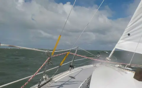 Vue depuis un voilier, mer agitée sous un ciel nuageux. Le gréement et la voile blanche sont visibles. Fiche technique du Challenger Scout.