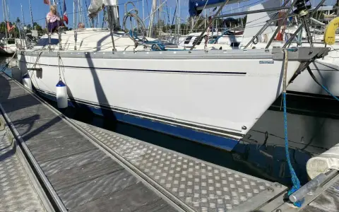 Un voilier blanc est amarré à quai. Le soleil se lève, projetant de longues ombres sur le ponton en bois.