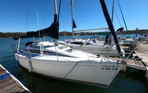 Voilier Beneteau First 235 blanc amarré à un ponton en bois, avec voiles noires et bleues.