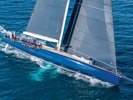 Un voilier bleu vif glisse sur l'eau, ses voiles sombres déployées comme un tapis volant 3. L'équipage est visible sur le pont.
