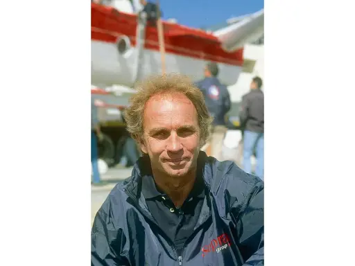 Jean-Claude Parisis, navigateur, souriant devant un avion rouge et blanc.