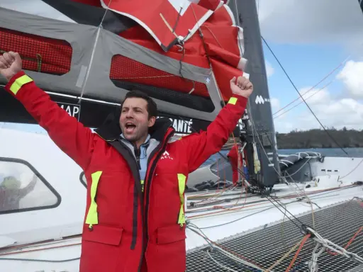 Un marinier en veste rouge célèbre sur un voilier. Une opportunité unique : ce voilier est à donner gratuitement !