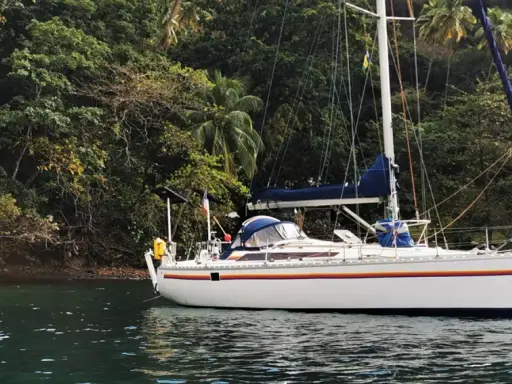 Voilier blanc ancré près d'une côte luxuriante et verdoyante. Le trismus 32 semble prêt pour une aventure tropicale.