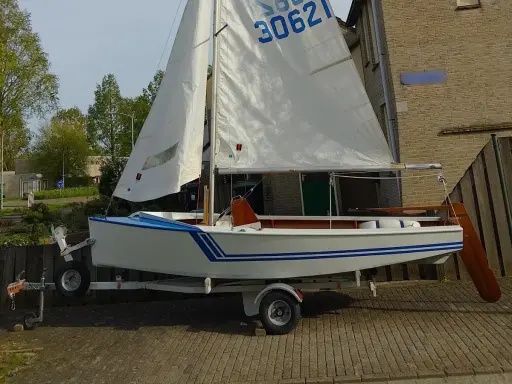 Un petit voilier blanc et bleu, un vaurien bateau prêt pour l'aventure, est sur sa remorque.