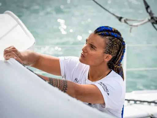 Marie Tabarly, concentrée, ajuste une voile sur son bateau. Ses tresses bleues et brunes flottent au vent.