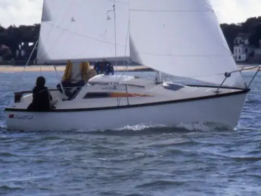 Voilier blanc naviguant sur une mer agitée, avec deux personnes à bord. Les premiers 18 avis sur ce modèle de bateau sont positifs.