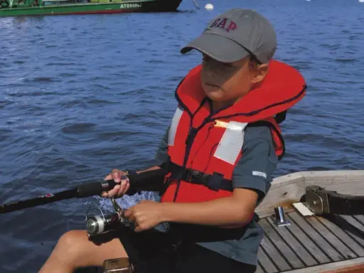 Un enfant pêche en mer, portant un gilet de sauvetage obligatoire. La question du gilet de sauvetage obligatoire jusqu'à quel âge est cruciale pour la sécurité nautique.