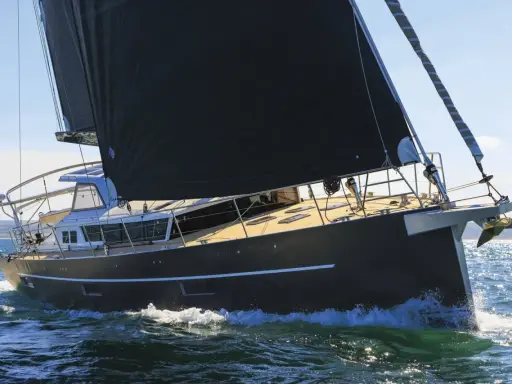Un voilier moderne, avec une grande voile noire, navigue sur une mer agitée. Xavier Desmarest admire la vue depuis le pont.