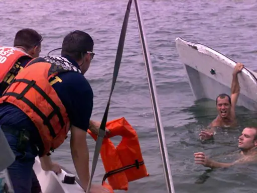 Sauvetage après un naufrage de bateau. Des secouristes en gilets orange aident des hommes dans l'eau, près d'une embarcation renversée.