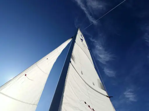 Voiles blanches gonflées par le vent, le bateau semble s'affaler sur l'eau bleue sous un ciel clair.