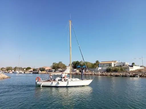 Un voilier atlante navigue sur des eaux calmes, avec des personnes à bord. Le ciel est bleu et dégagé.