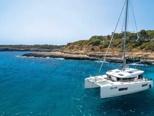 Un catamaran blanc, le "StarElli", navigue dans des eaux turquoise près d'une côte rocheuse et verdoyante. Ce safran catamaran offre une vue idyllique.