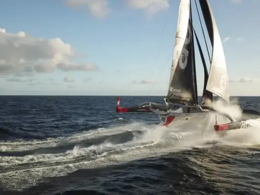 Le trimaran "Actual" d'Yves Le Blevec fend les vagues, propulsé par le vent sous un ciel bleu.