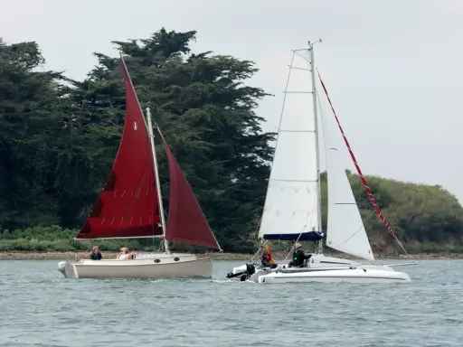 Deux voiliers naviguent sur l'eau, l'un avec une voile rouge, l'autre avec une voile blanche. On dirait un **bateau corsaire** prêt pour l'aventure.