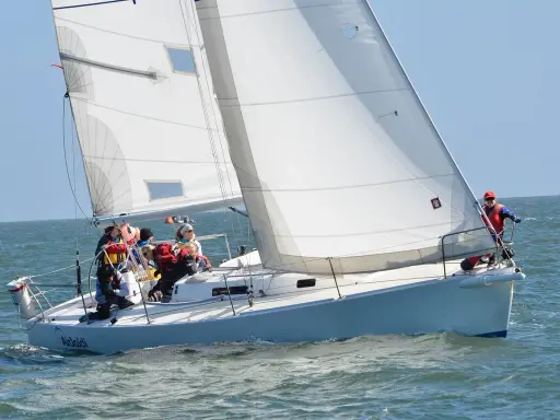 Équipage concentré sur un foc voilier blanc, naviguant sur une mer agitée sous un ciel bleu clair.