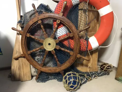 Roue de gouvernail en bois, filet de pêche, bouée de sauvetage orange et pagaies évoquent un safran de bateau prêt pour l'aventure.