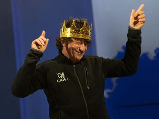 Jean Le Cam, le roi des mers, porte une couronne dorée et une veste noire avec l'inscription "YES WE CAM L".