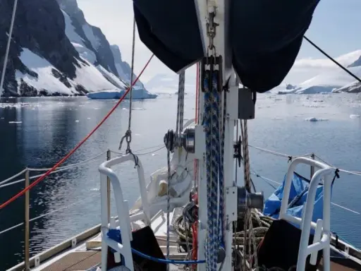 Voile sur un voilier dans un fjord glacé, avec des montagnes enneigées et des icebergs. Le **pen duick 600** navigue paisiblement.