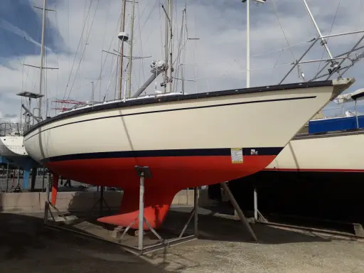 Voilier Dufour 31 sur bers. La coque est crème avec une bande bleue et une quille rouge vif.