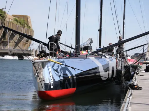 L'IMOCA Charal, un voilier de course futuriste, est amarré à quai. Des marins s'affairent sur le pont, préparant le navire pour une nouvelle aventure en mer.