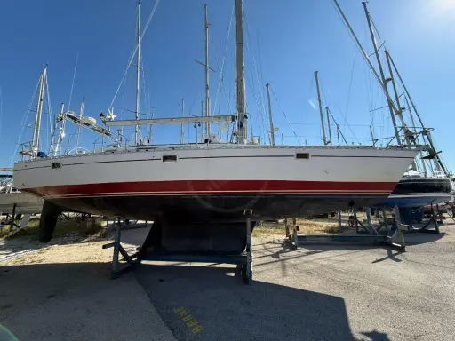 Un voilier blanc et rouge, prêt pour l'aventure, est exposé sur des bers. Ce navire, un modèle de **Gibert Marine**, attend de retrouver les flots.