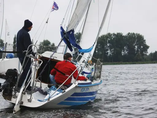 Deux hommes naviguent sur un voilier micro challenger, le vent gonflant les voiles sur un lac calme.