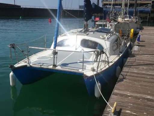 Un catamaran Hirondelle bleu et blanc, amarré à un ponton en bois, prêt pour une nouvelle aventure sur l'eau.