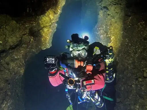 Plongée dans une grotte sous-marine, Xavier Meniscus filme les parois rocheuses éclairées par ses lampes.