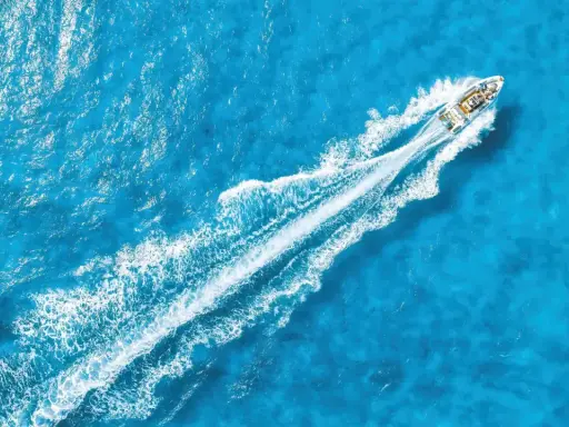 La coque d'un bateau fend les eaux bleues, laissant une traînée blanche de mousse.