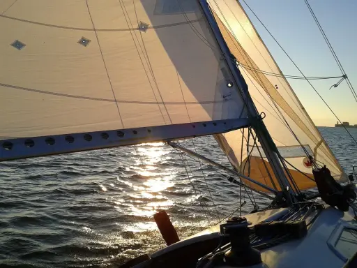 Voile d'un bateau au coucher du soleil, reflets dorés sur l'eau. La balancine du bateau est bien tendue.