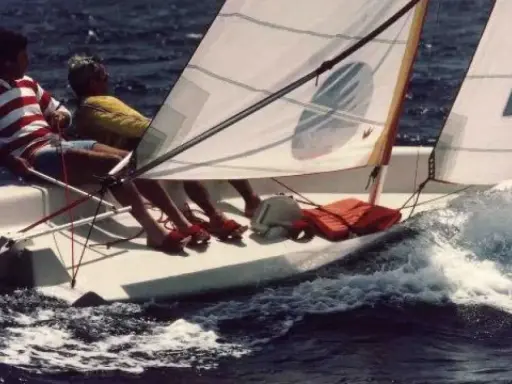 Deux personnes naviguent sur un dériveur Wizz, le bateau fend les vagues dans une joyeuse course.
