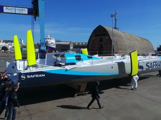 Équipe poussant un **60 pieds IMOCA** de course au large, le Safran, dans un chantier naval.