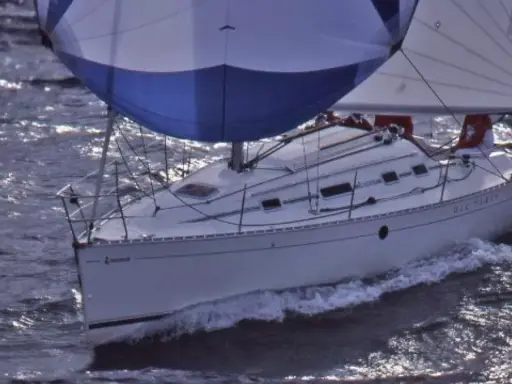 Voilier blanc naviguant sur des eaux agitées, ses voiles bleues et blanches gonflées par le vent. Le nom "DIE-TERRY" est visible sur la coque.