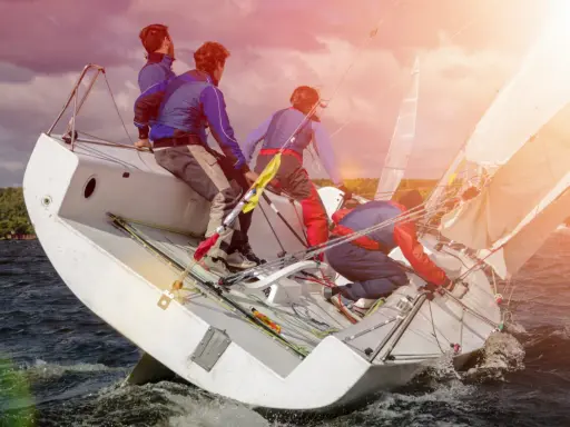 Équipe en pleine action pour apprendre la voile. Le voilier est incliné, les marins ajustent les voiles sous un ciel orageux.
